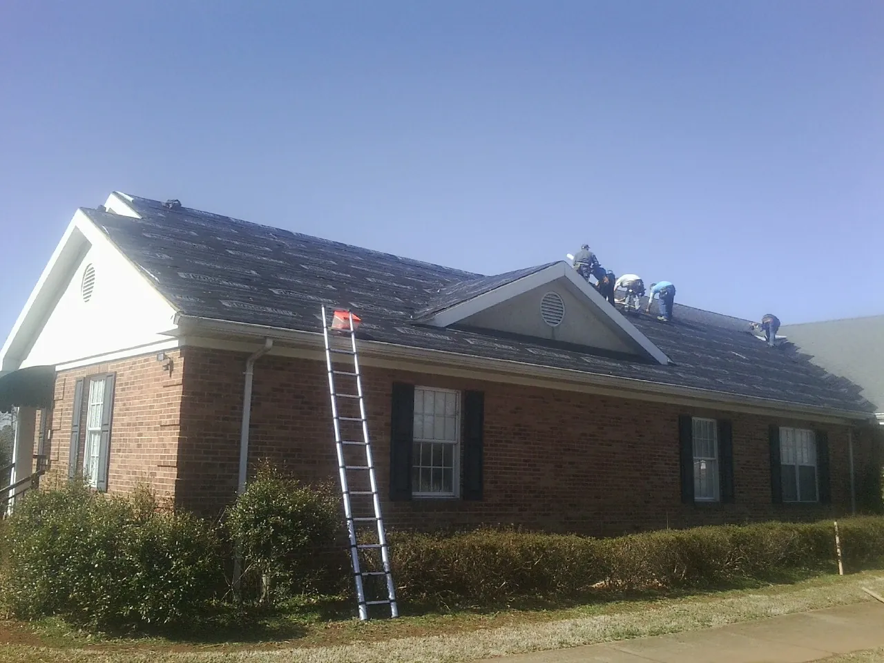 Crew tearing shingles off a brick ranch roof with a ladder set — Emergency Roof Repair work by our crew in Robersonville