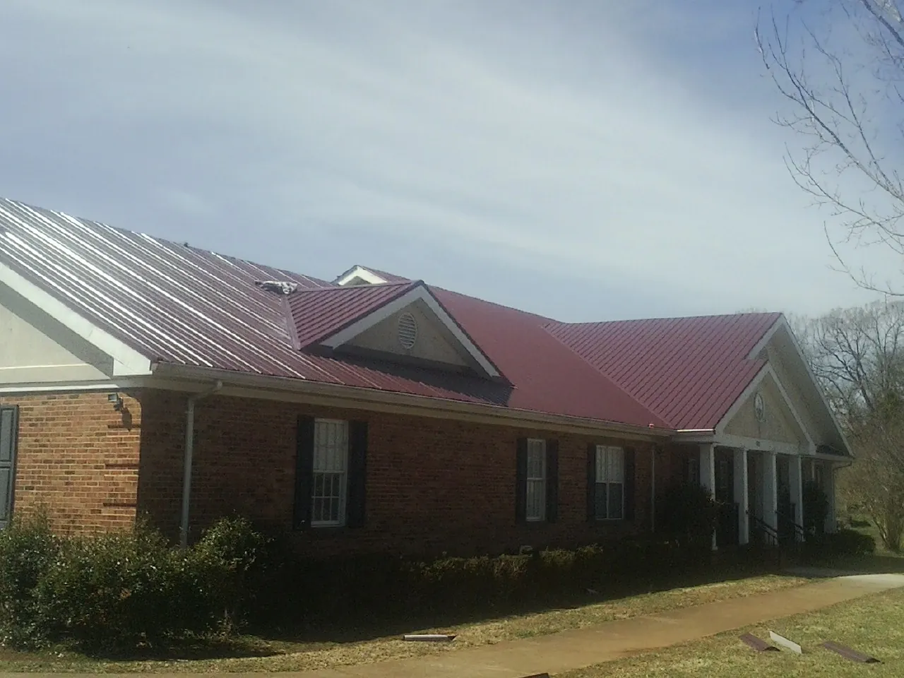 Red metal roof with gabled entries on a long brick building, from a Hail Damage Roof Repair job in Robersonville