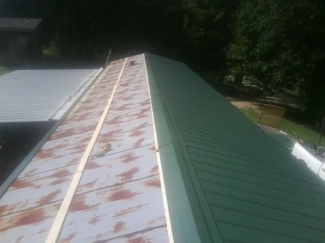 Old rusted panels beside newly installed green metal roofing — Wind Damage Roof Repair by Roofing Brothers in Robersonville