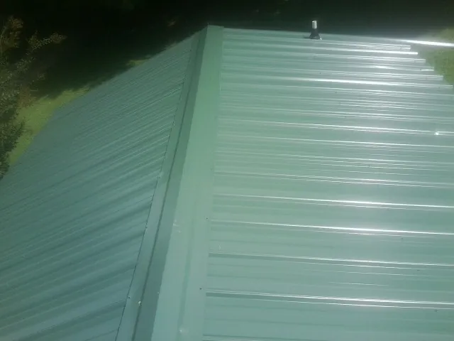 New green metal panels meeting at the ridge of a roof — Flat Roof Repair work by our crew in Robersonville