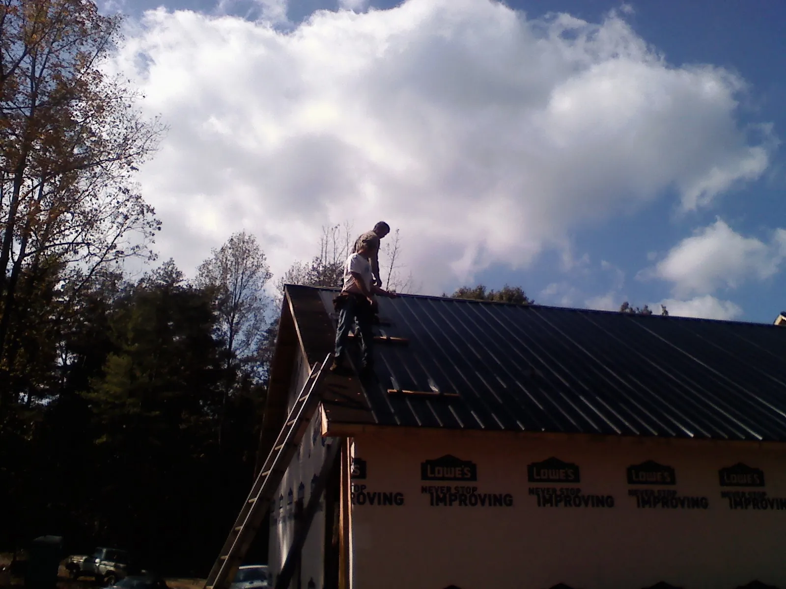 Roofer fastening dark metal panels high against a cloudy sky, from a Roof Inspection job in Robersonville