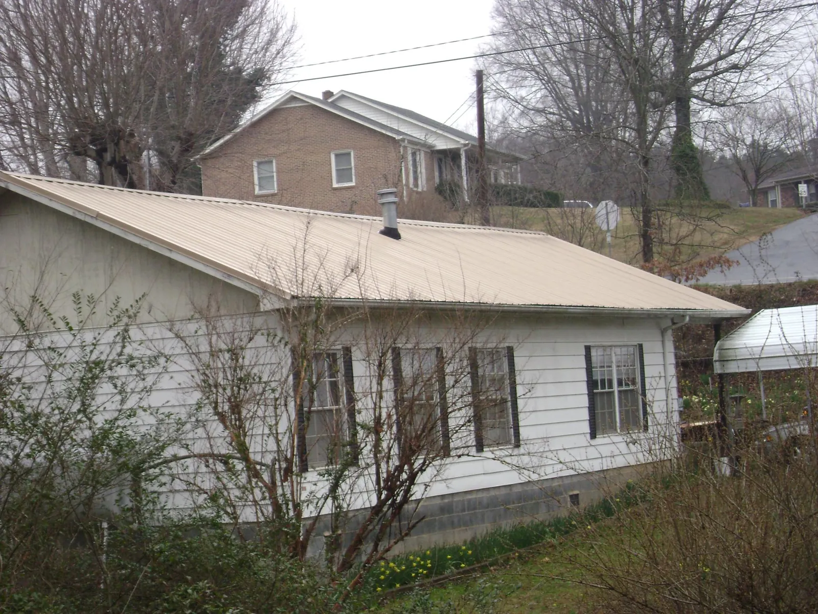 Tan metal roof on a white sided house set into a hillside — Commercial Roofing by Roofing Brothers in Robersonville