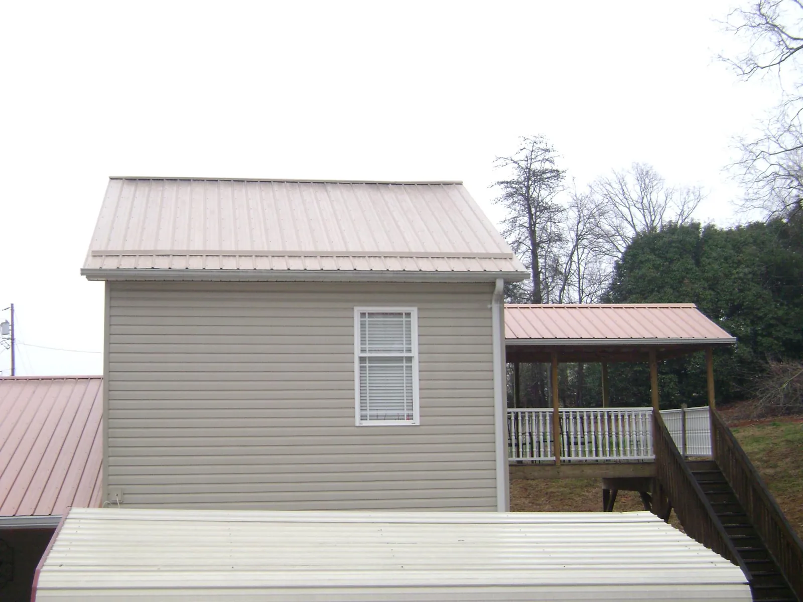 Tan metal roofs on a two story addition and attached porch, from a Roof Replacement job in Robersonville